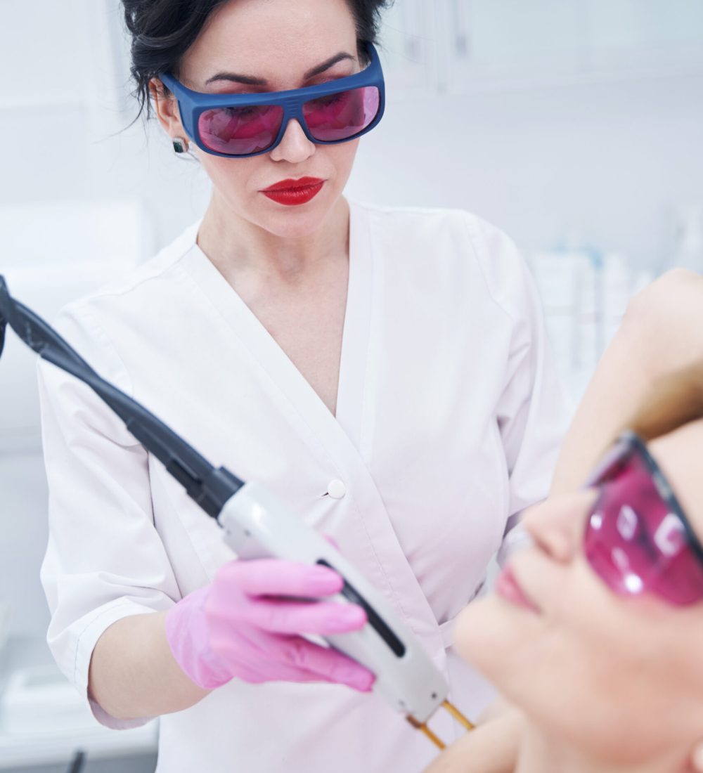 Female cosmetologist in safety glasses removing hair from woman armpit with alexandrite laser machine