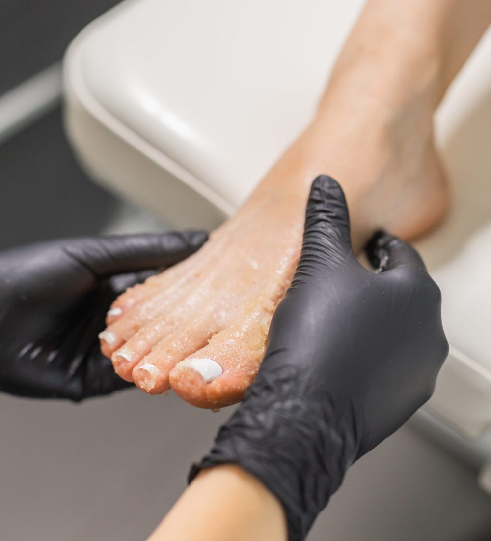 Woman doing foot peeling in pedicure SPA salon. Sugar scrub and relax beauty procedure.